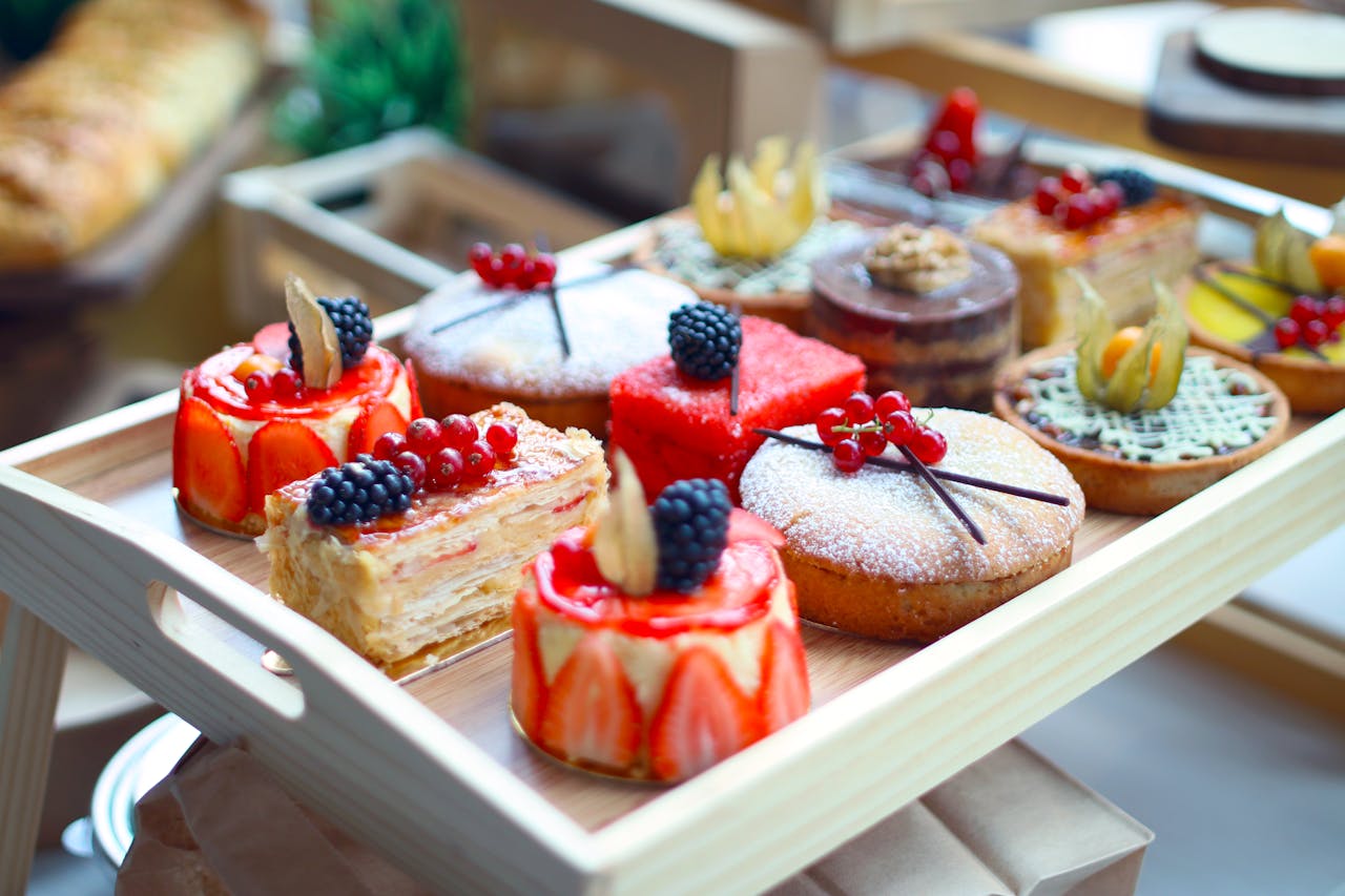 Close-up of a variety of beautifully crafted pastries on a wooden tray, showcasing vibrant colors and intricate details.